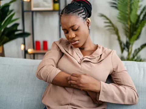Woman sitting on a couch scratching her arm.