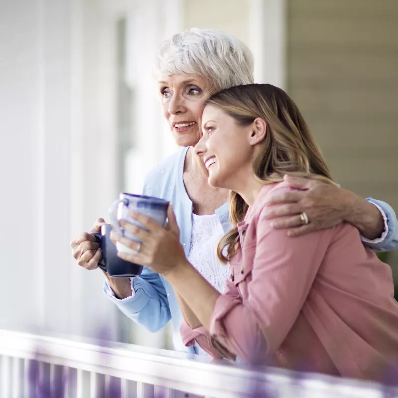 Two women converse on the front porch while drinking coffee.