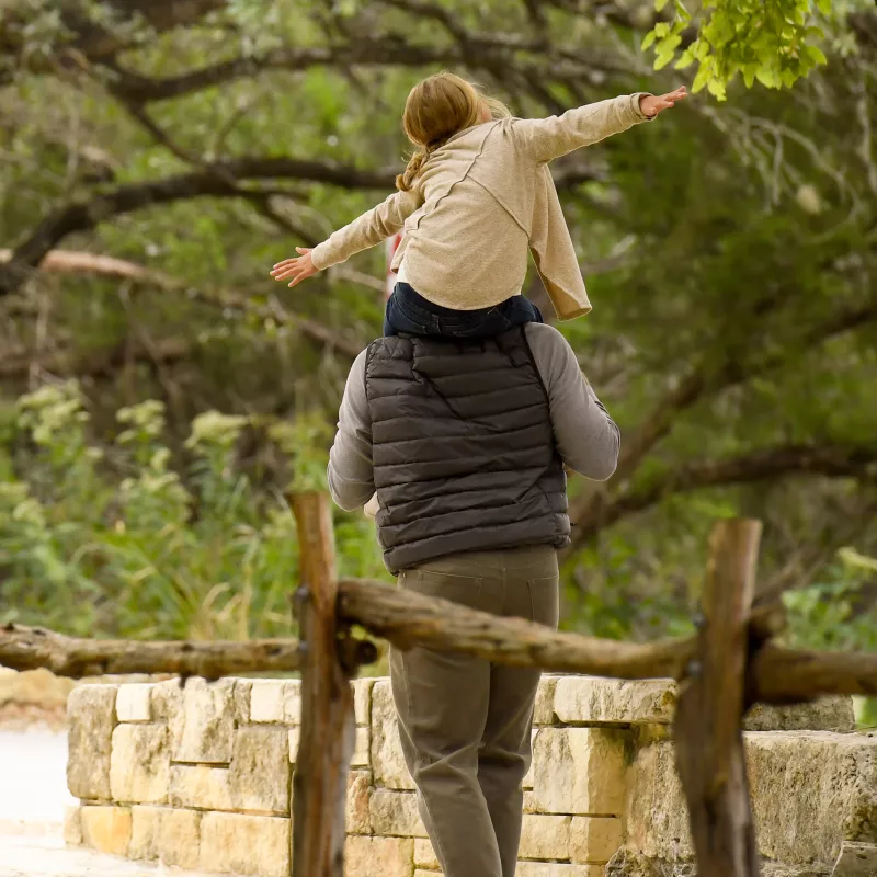 Father and daughter walking in the woods next to a fence.