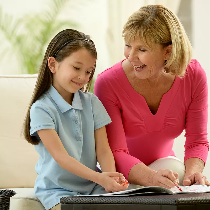 A grandmother colors with her granddaughter on the couch.