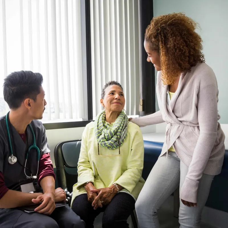 A woman sitting in a waiting room is comforted by a friend while an AdventHealth physician sits by her side.