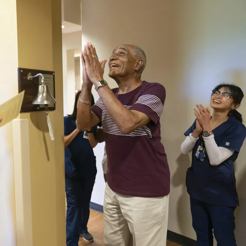 Male patient and care team celebrating after ringing cancer-free bell.