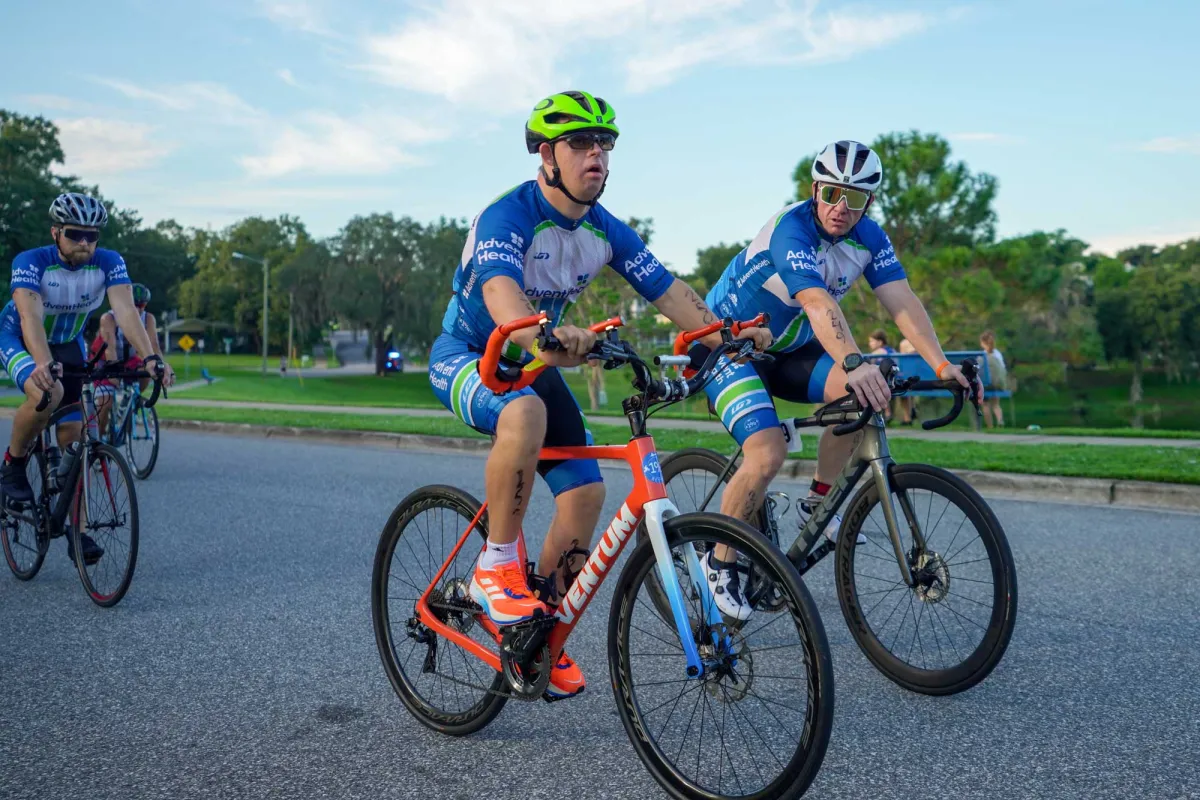 Triathlon participant, Chris Nikic, and his physical therapist, Trevor Hicks, biking on the road