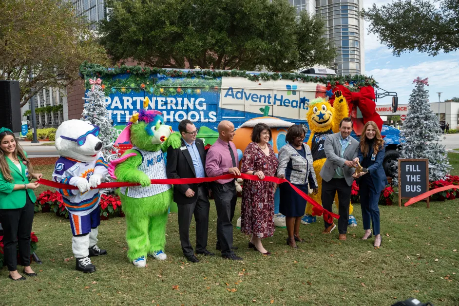AdventHealth and partners from the Orlando Magic, Florida Citrus Sports, Second Harvest Food Bank and local school districts cut the ribbon on AdventHealth's "Drive Out Hunger" Holiday Bus.