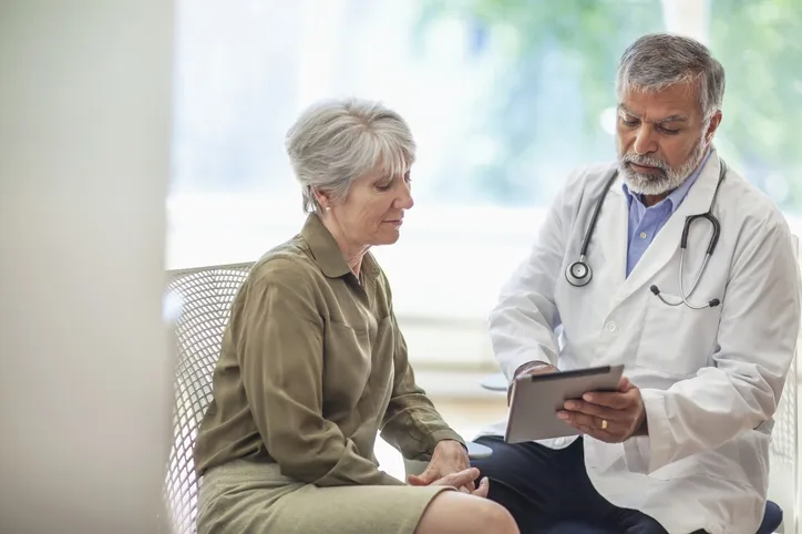 senior man doctor medical professional talks using digital tablet to senior woman in health clinic - stock photo