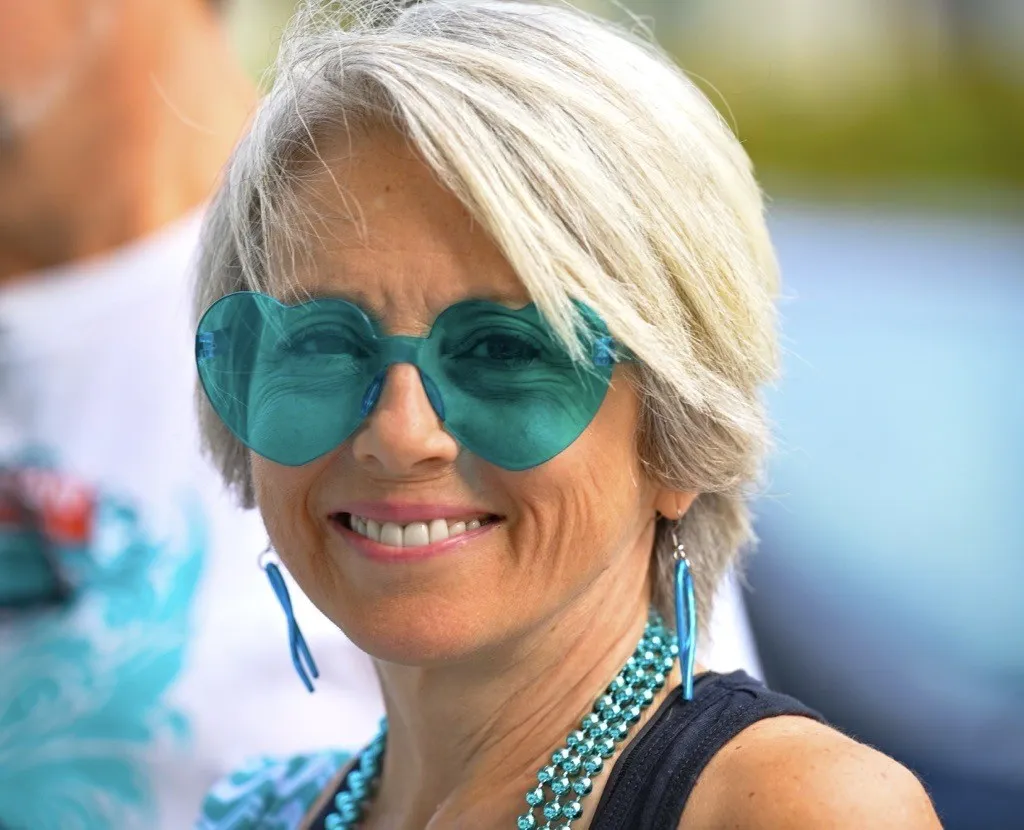 Anita Robinson, a woman with short blonde hair and tan skin, wearing teal heart-shaped sunglasses