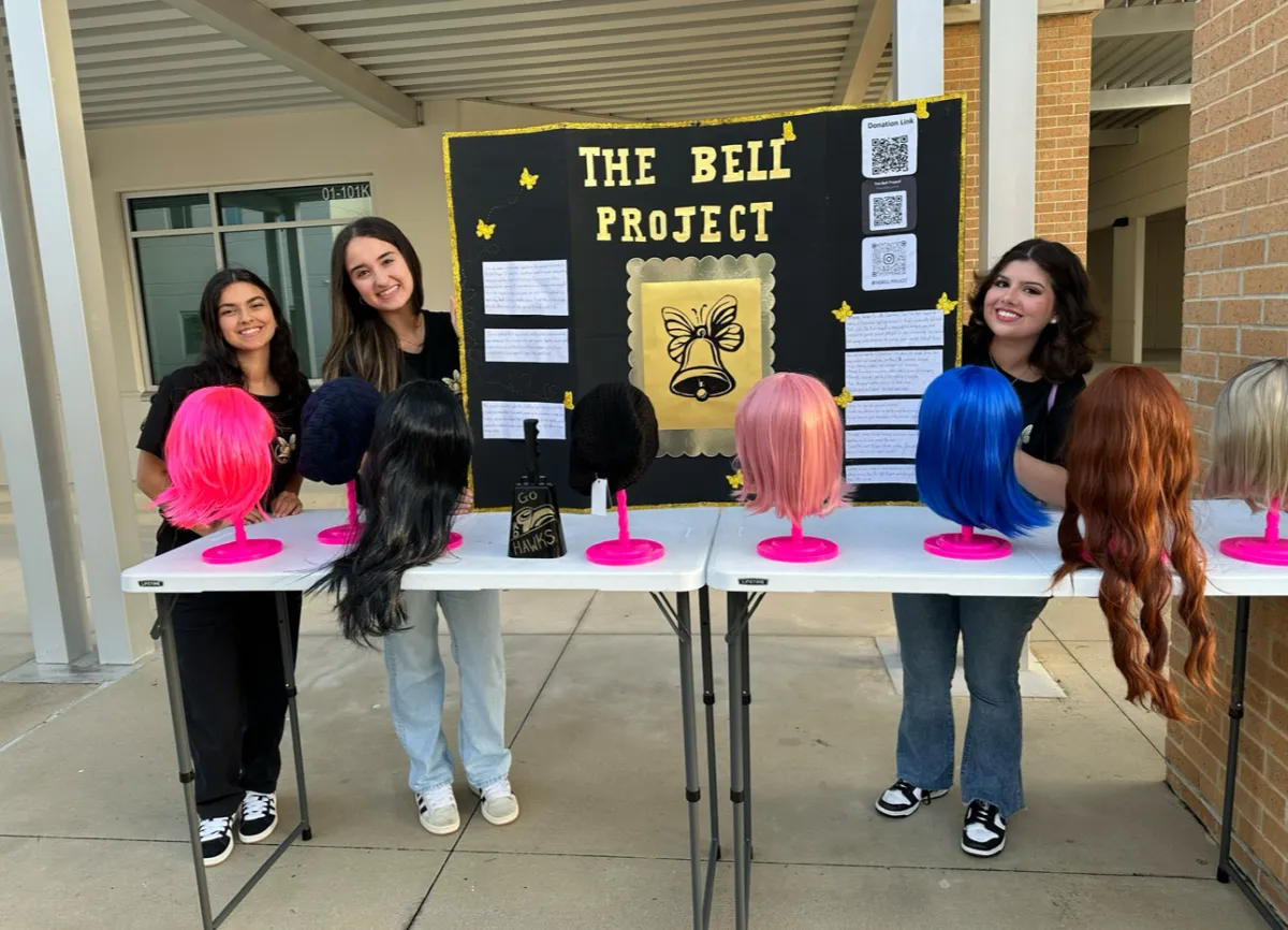 Julia and two members of the Bell Project beside a sign and a few wigs.