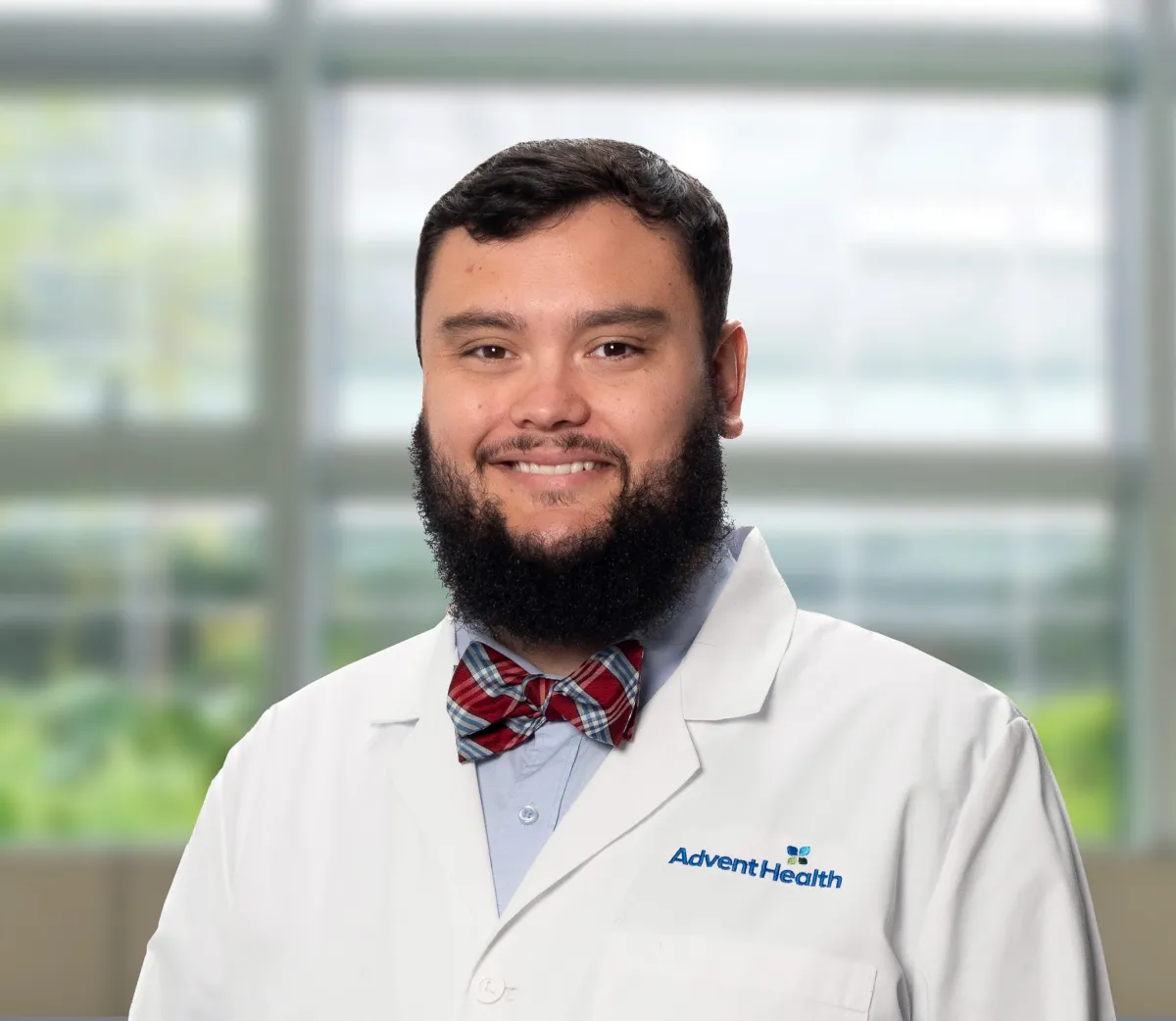 Jacob Parker, a dark-haired, bearded white man in a white medical coat, stands smiling in front of a blurred office-style background.