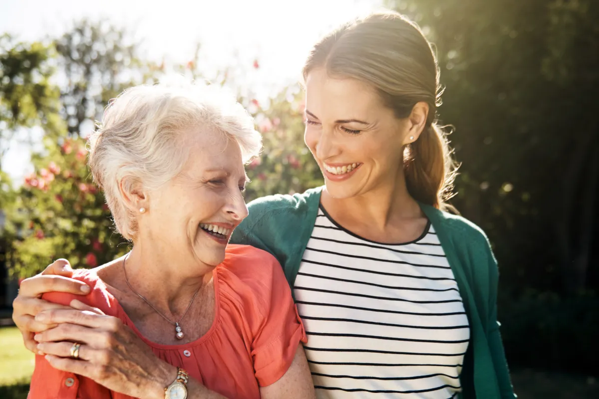 A senior woman with her adult daughter walking together outdoors.