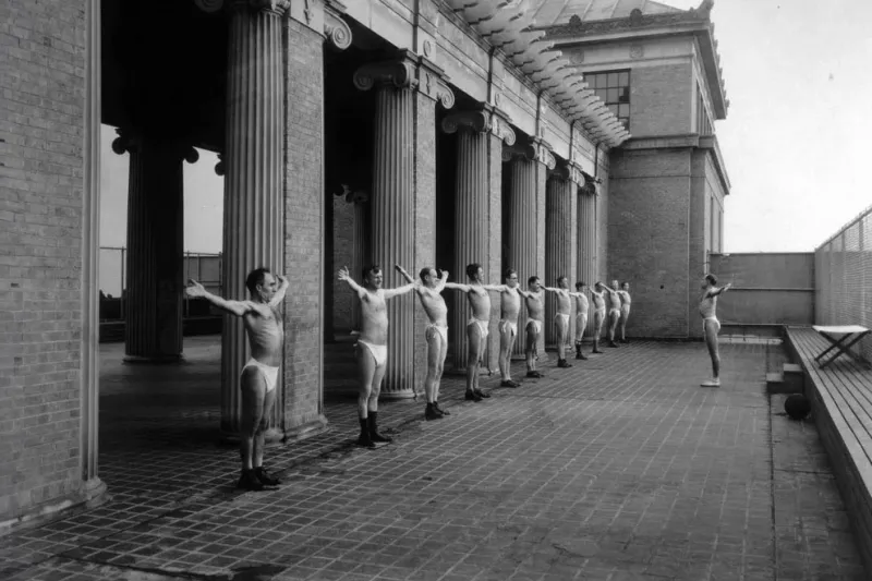 A black and white image of male patients standing outdoors in the sun.