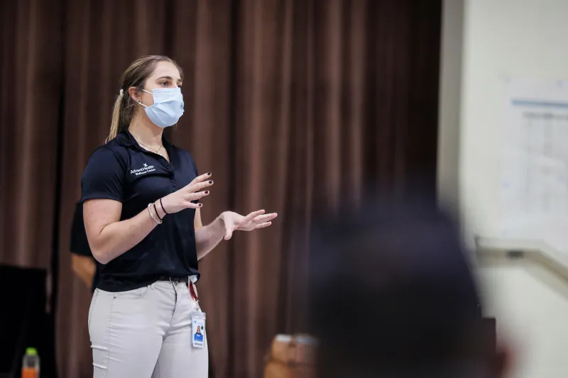 A masked woman on a stage giving a presentation