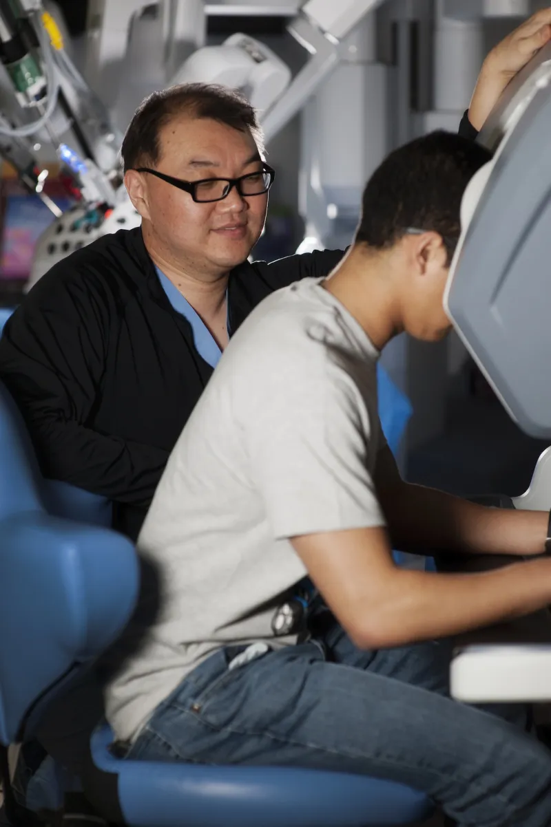 Two men looking at a robotic surgery control station.