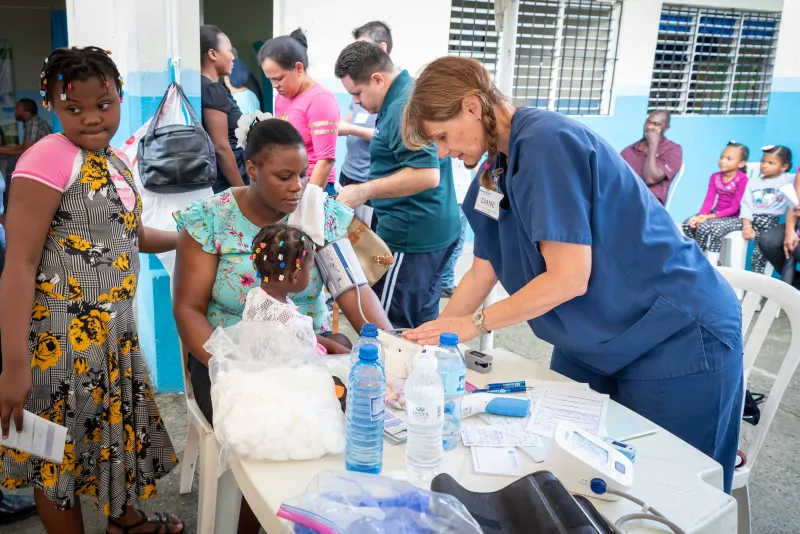 Doctor checking woman's blood pressure while her children are near here.