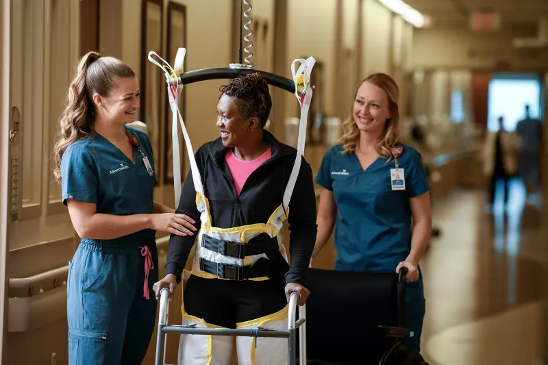 A woman walking with the help of two healthcare workers.